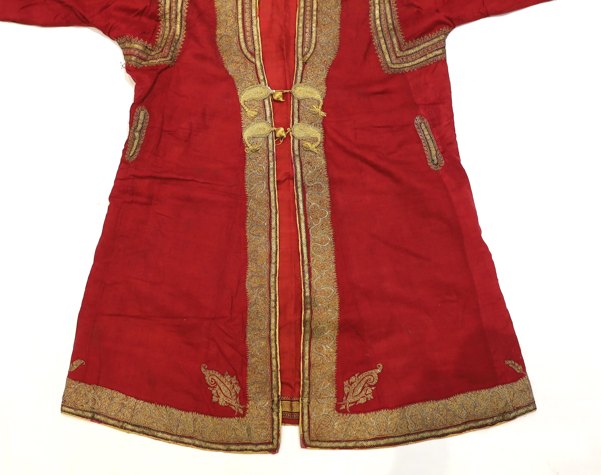 A late 19th century gentleman’s quilted red silk Indian Chogha, embroidered with ornate gold and silver metallic thread borders and paisley design details